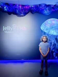 Boy standing in front of Jellyfish Museum sign with large glowing jellyfish installation, Pompano Beach Florida