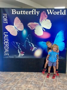 Young twins standing in front of the Butterfly World Fort Lauderdale entrance sign in Coconut Creek, Florida
